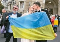 烏克蘭收復赫松市，一對新人十二日在敖德薩拉開國旗同表歡慶。（美聯社）